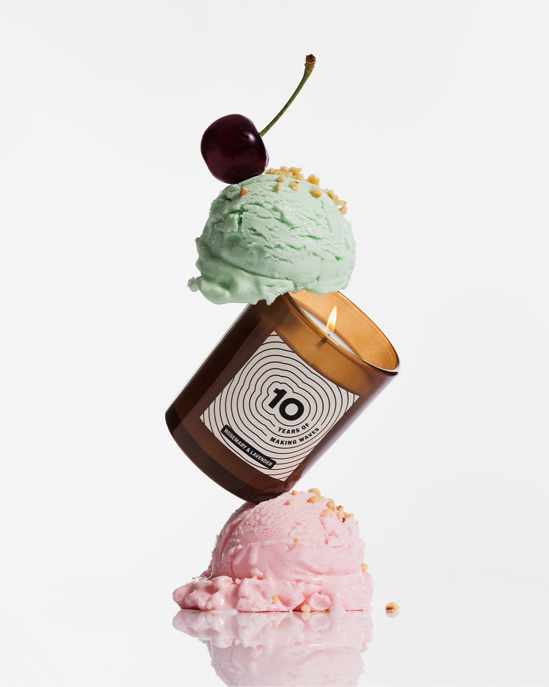Candela marrone bilanciata tra due palline di gelato pastello, con una ciliegia in cima.