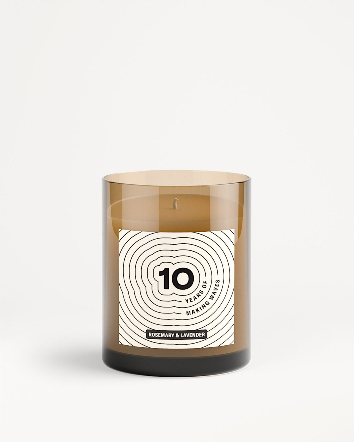 Vaso di vetro marrone per candela con etichetta bianca e motivo a cerchi concentrici.