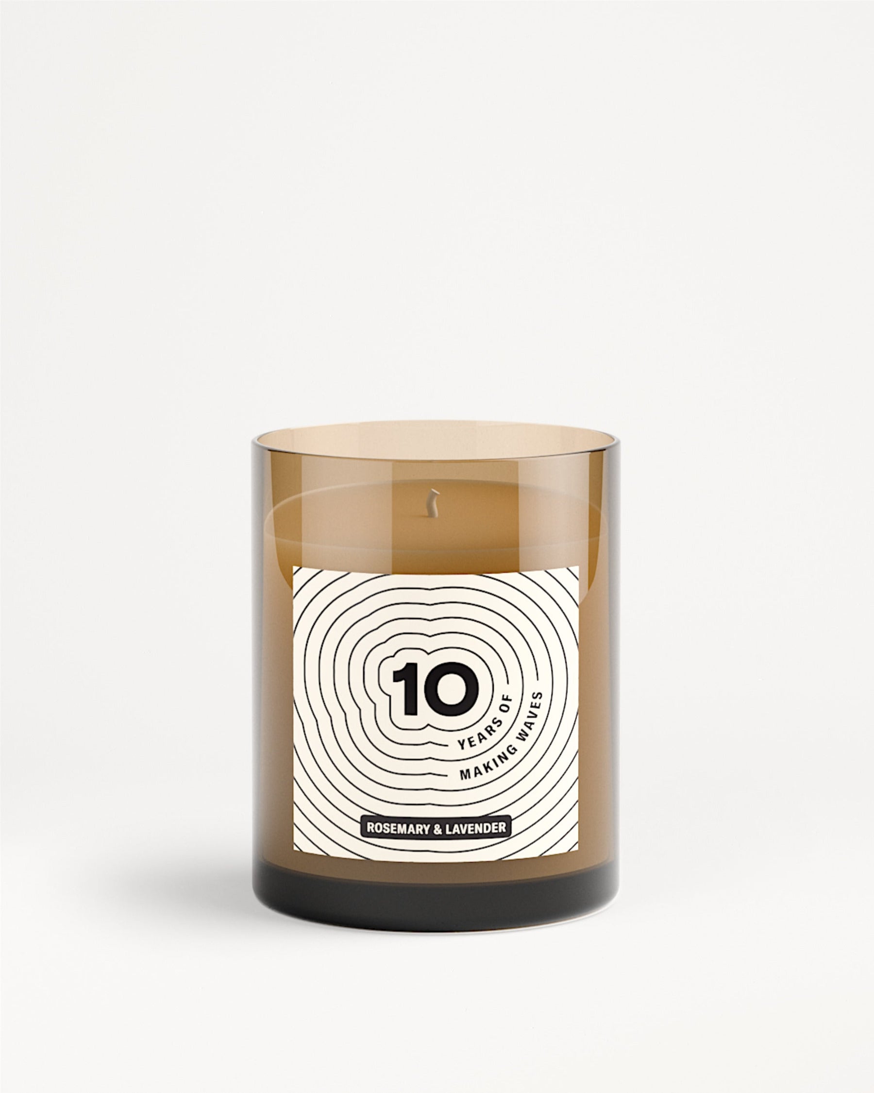 Vaso di vetro marrone per candela con etichetta bianca e motivo a cerchi concentrici.