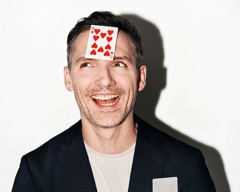 Uomo sorridente con una carta sulla fronte, sfondo bianco.