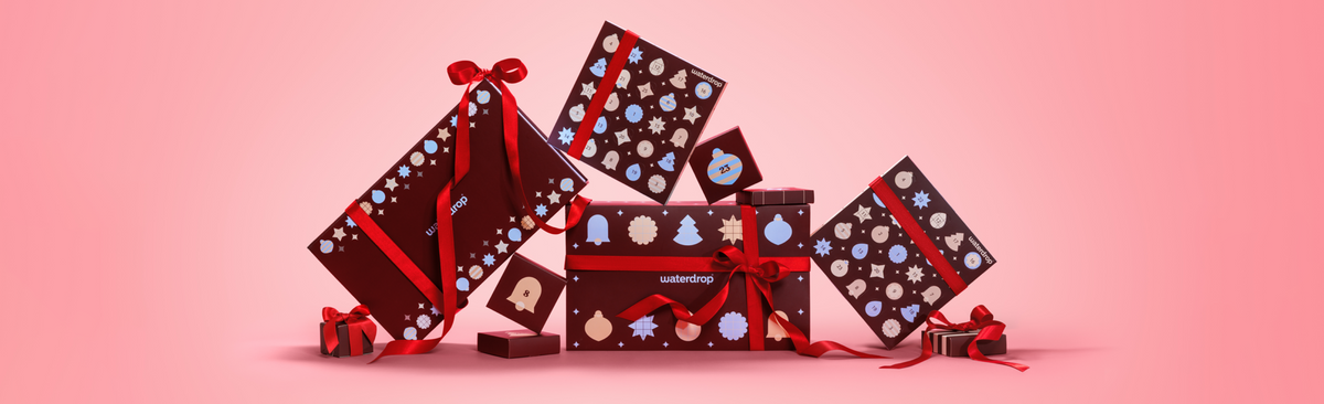 Scatole regalo colorate disposte in una composizione festosa su sfondo rosa sfumato.
