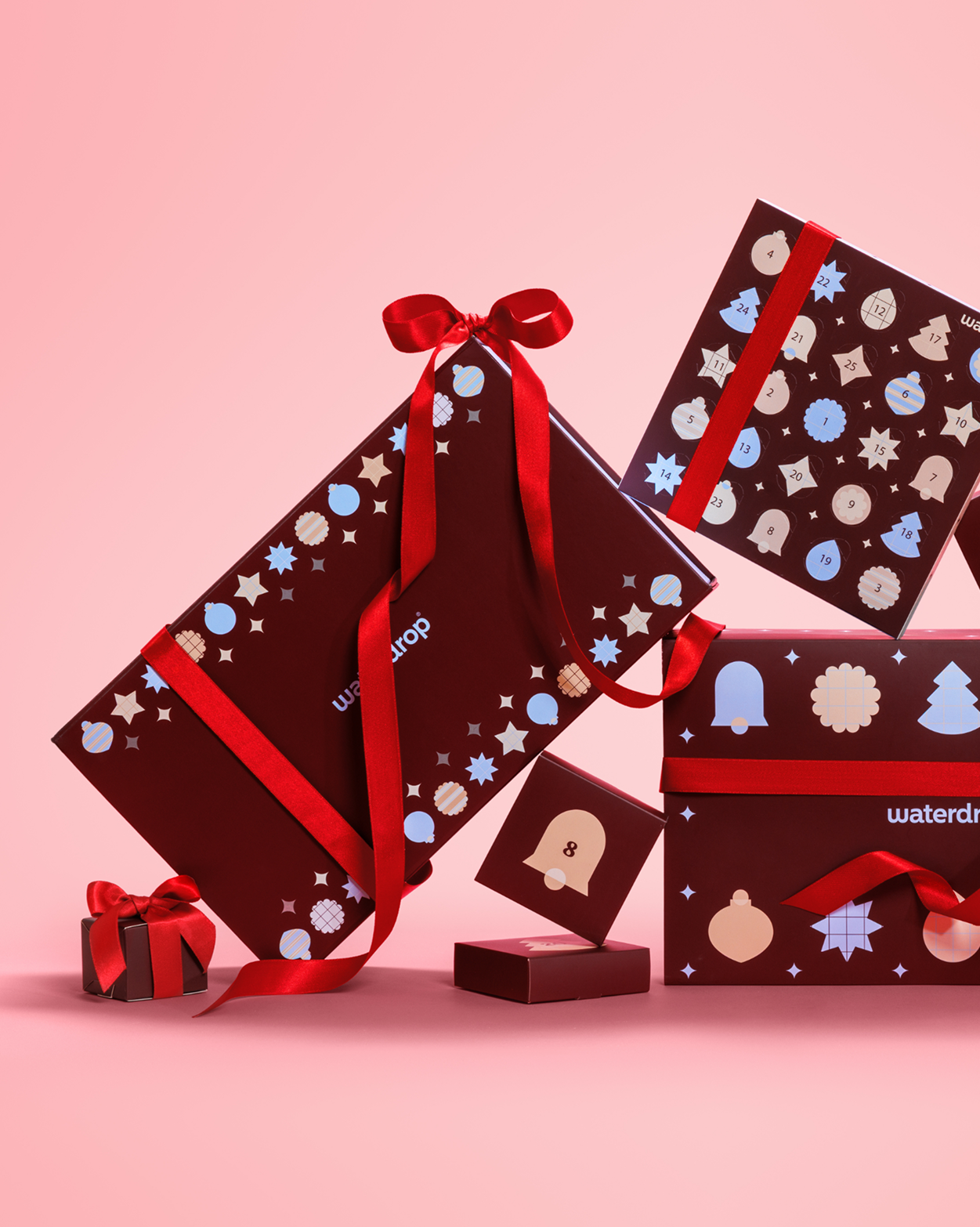 Scatole regalo incartate con nastri rossi e motivi festivi su sfondo rosa.