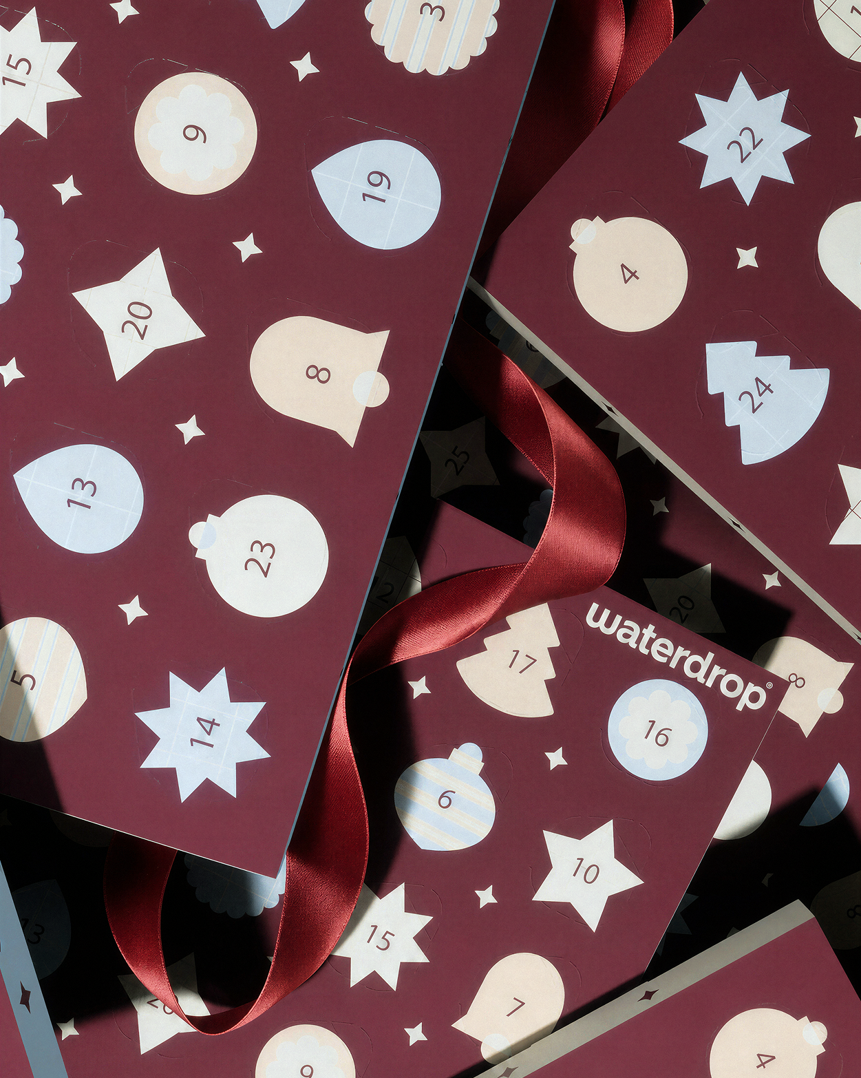 Calendario dell'Avvento con porte numerate su pannelli bordeaux e nastri rossi.