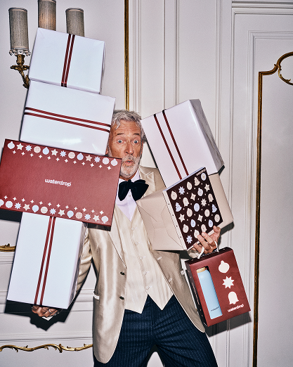 Uomo in completo beige che porta diverse scatole regalo incartate all'interno.