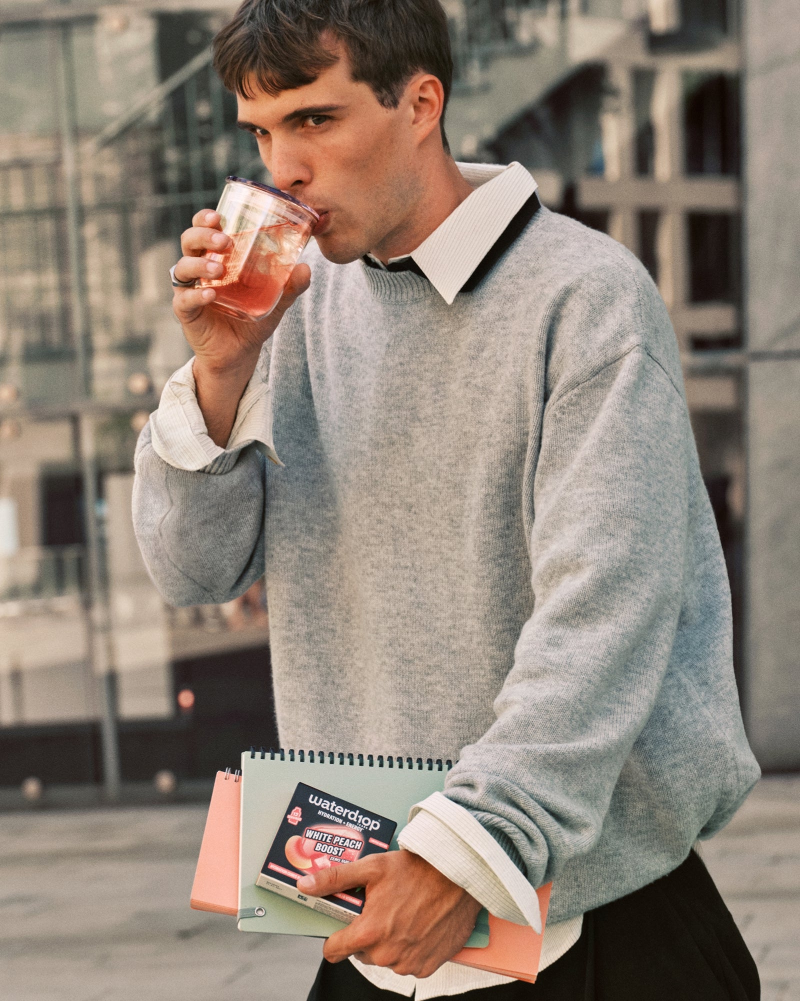 Uomo in pullover grigio che beve da una tazza mentre porta quaderni.