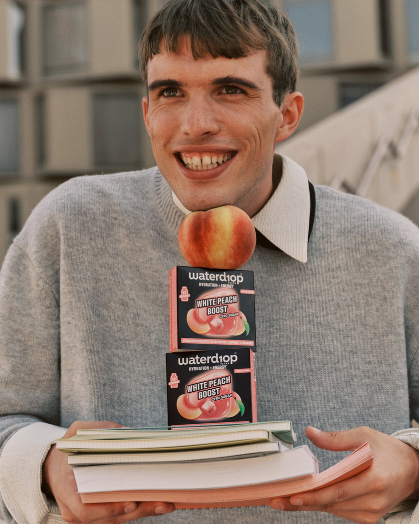 Giovane uomo in pullover grigio che tiene due confezioni al gusto pesca su una pila di libri.