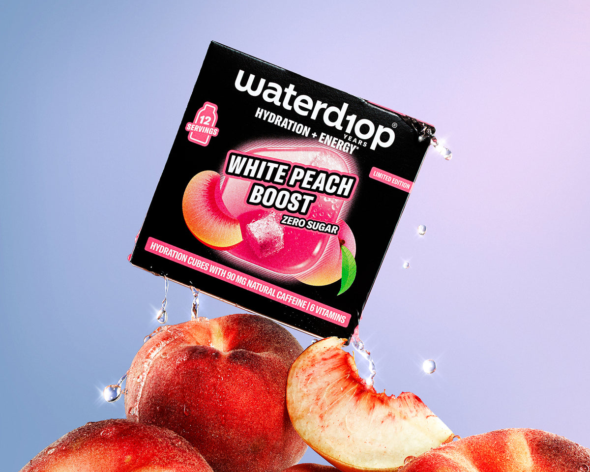 Scatola di prodotto idratante ed energetico posata su un mucchio di pesche con gocce d’acqua, sfondo gradiente rosa e blu.