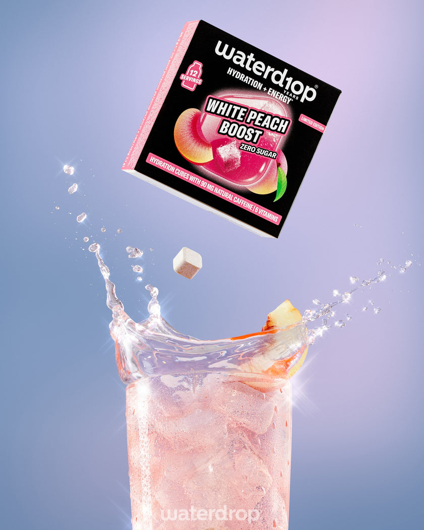 Una confezione cade verso un bicchiere alto di bevanda pink al gusto pesca, con pezzi di pesca, creando una spruzzi.