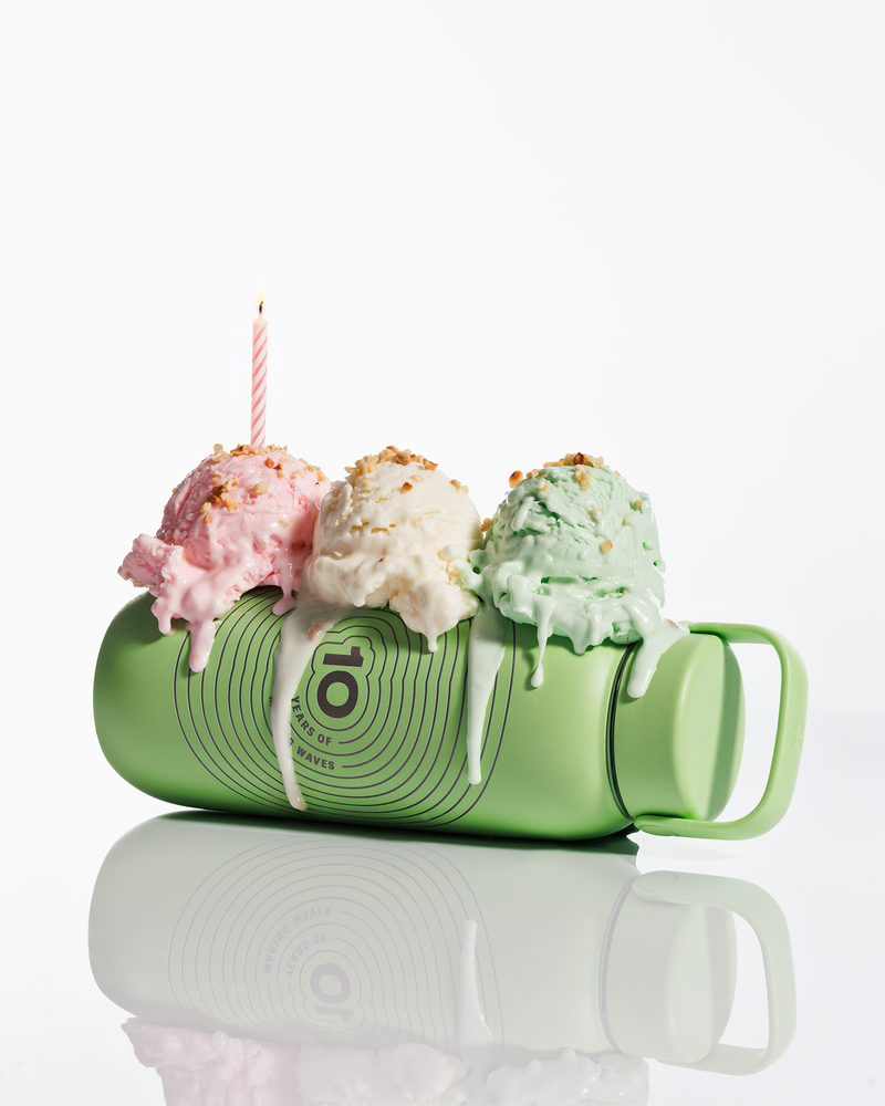 Una tazza verde inclinata con tre palline di gelato sulla sommità e una candela accesa, con sciroppo che cola.