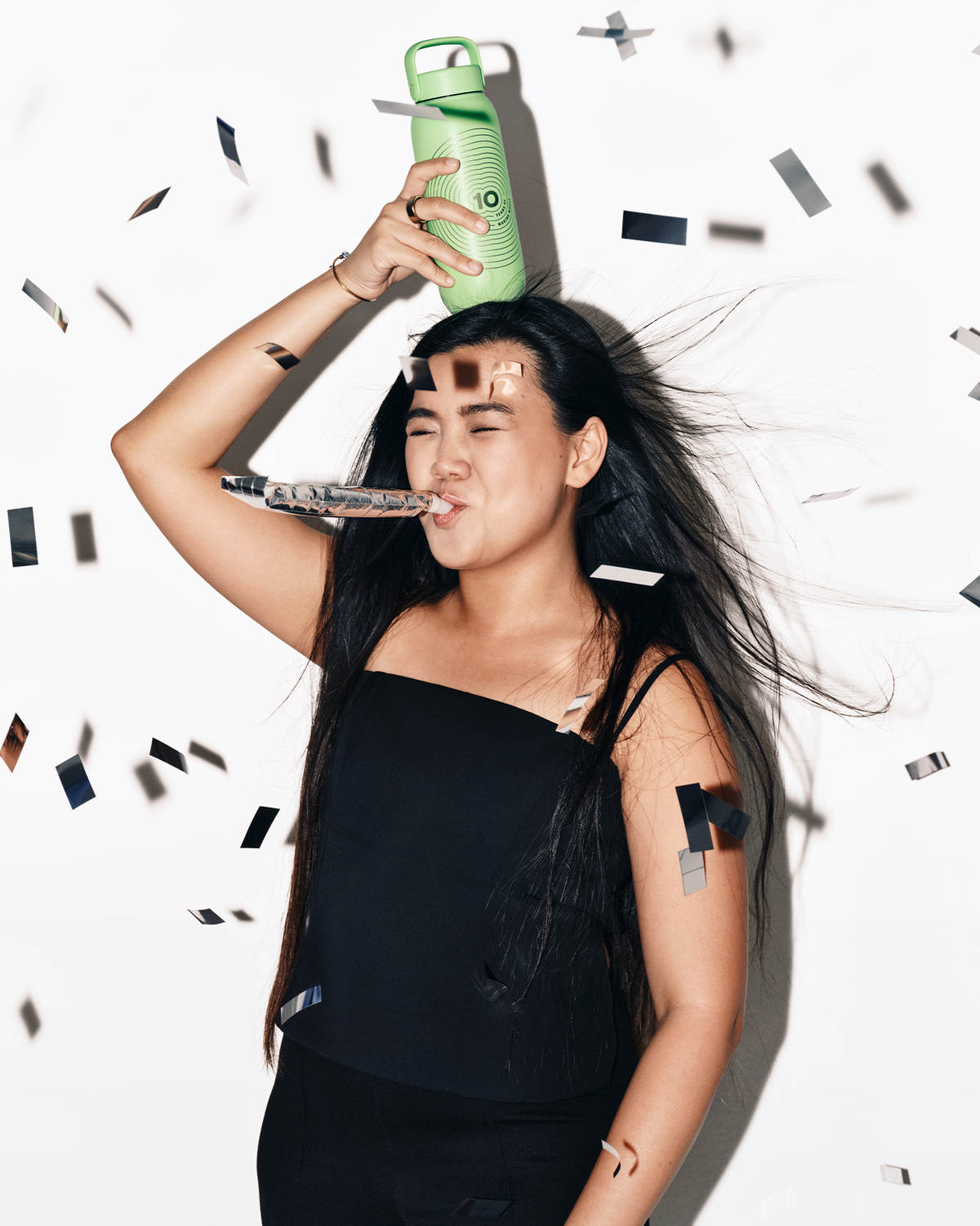 Donna in top nero tiene una bottiglia spray verde sulla testa mentre i confetti cadono intorno.