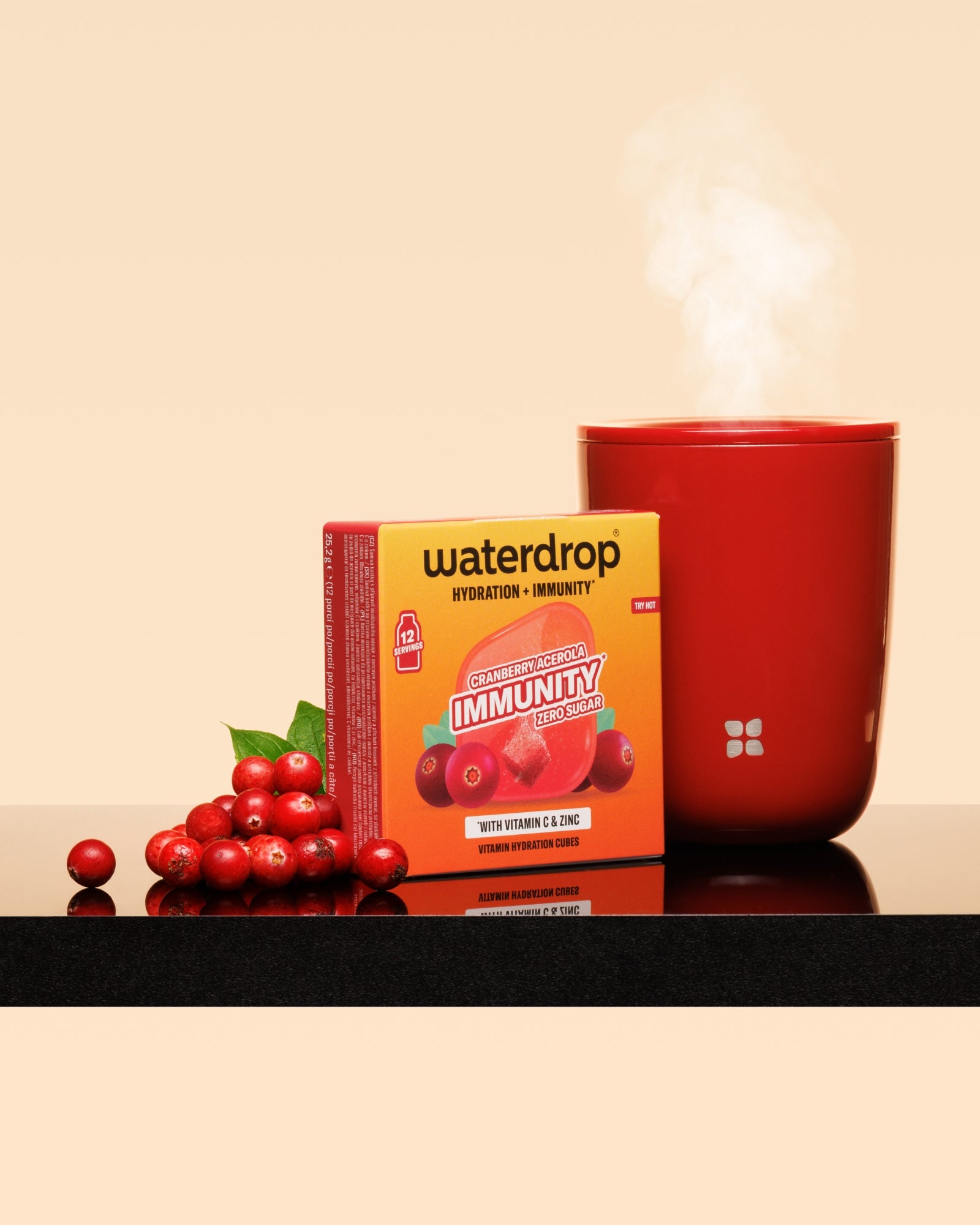 Tazza rossa fumante accanto a una scatola rossa e un grappolo di mirtilli su una superficie lucida.
