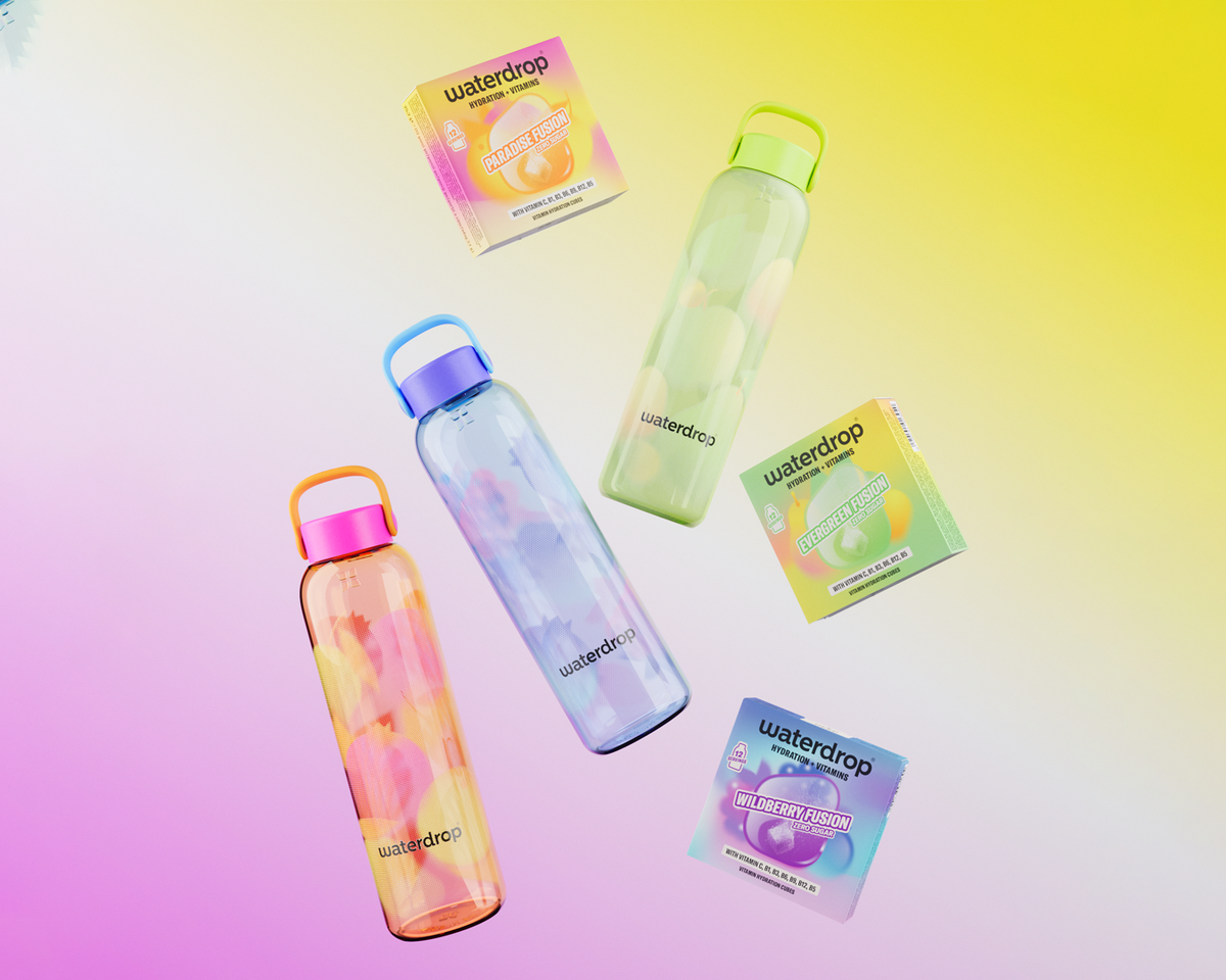 Set di quattro bottiglie d'acqua riutilizzabili trasparenti con tappi colorati, su uno sfondo pastello, accanto alle confezioni.
