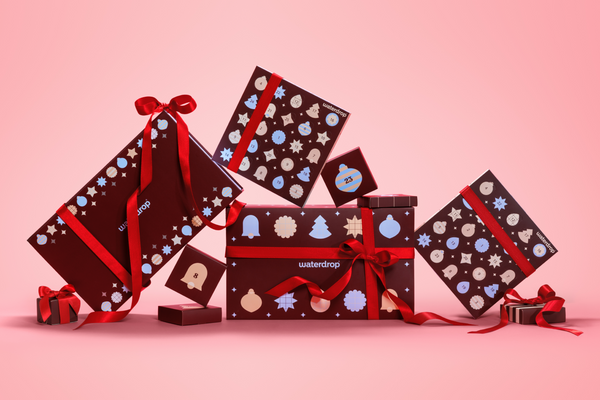 Scatole regalo assortite avvolte in carta scura con nastri rossi su uno sfondo rosa sfumato.