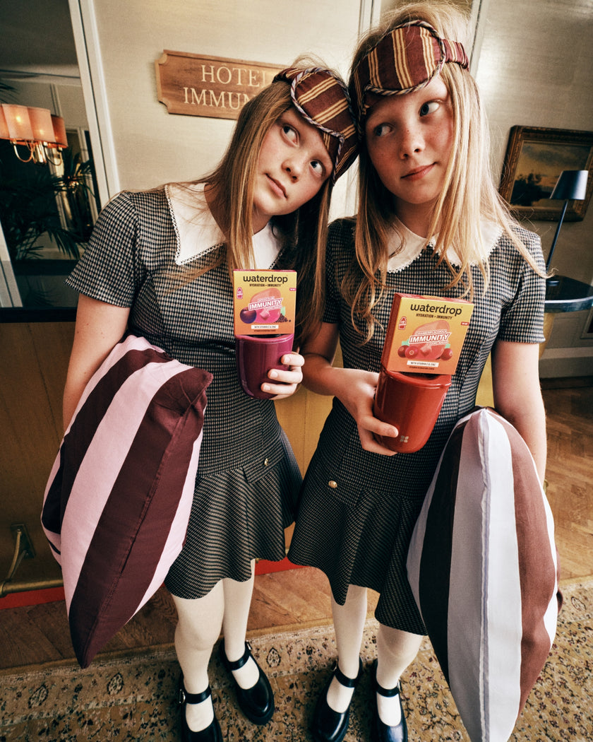 Due ragazze vestite con abiti grigi coordinati con colli bianchi tengono bevande al succo in una hall dell'hotel.